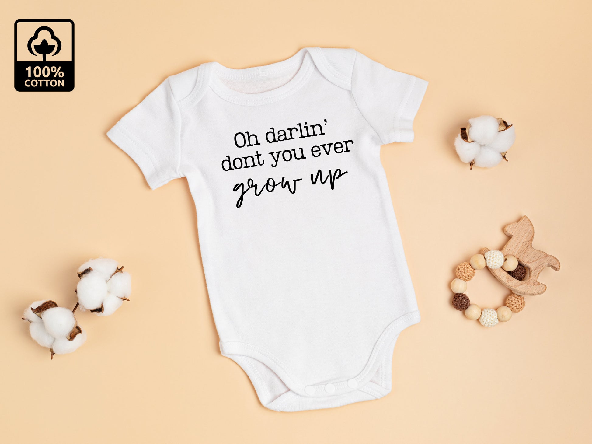 A white baby bodysuit with the text 'Oh Darlin' don't you ever grow up' printed on the front. The perfect piece of unisex taylor inspired baby clothing.